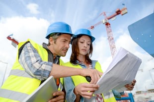 man and woman looking at architecture drawings on a construction site